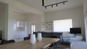 A modern living room with a wooden dining table, grey sofa, and a TV on a stand. - Beautiful 3-bed House in Chania With Garden (Platanias)
