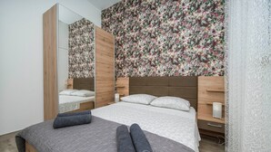 A modern bedroom with a large bed, wooden headboard, floral wallpaper, and a mirror. - Holiday Home Relax (Podstrana)