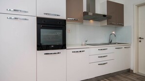 A modern kitchen with white cabinets, a black oven, a stainless steel range hood, and a sink with a faucet. - Holiday Home Relax (Podstrana)