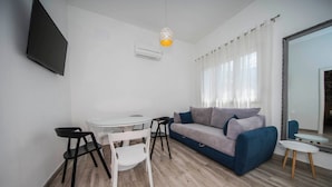 A modern living room with a sofa, a dining table, chairs, a TV, and a mirror. - Holiday Home Relax (Podstrana)