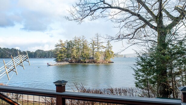 A lakeside view from a deck with a railing, a dock, and a small island with trees. - Waterfront home sleeping 10 located on Cummings Cove on Lake Winnipesaukee (Meredith)