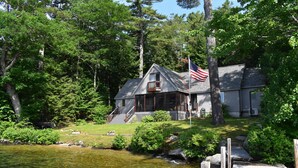 A cabin with a dock, surrounded by dense forest and a small stream. - Waterfront home sleeping 10 located on Cummings Cove on Lake Winnipesaukee (Meredith)