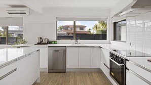Uma cozinha moderna com armários brancos, lava-louças, fogão e janela com vista para casas.