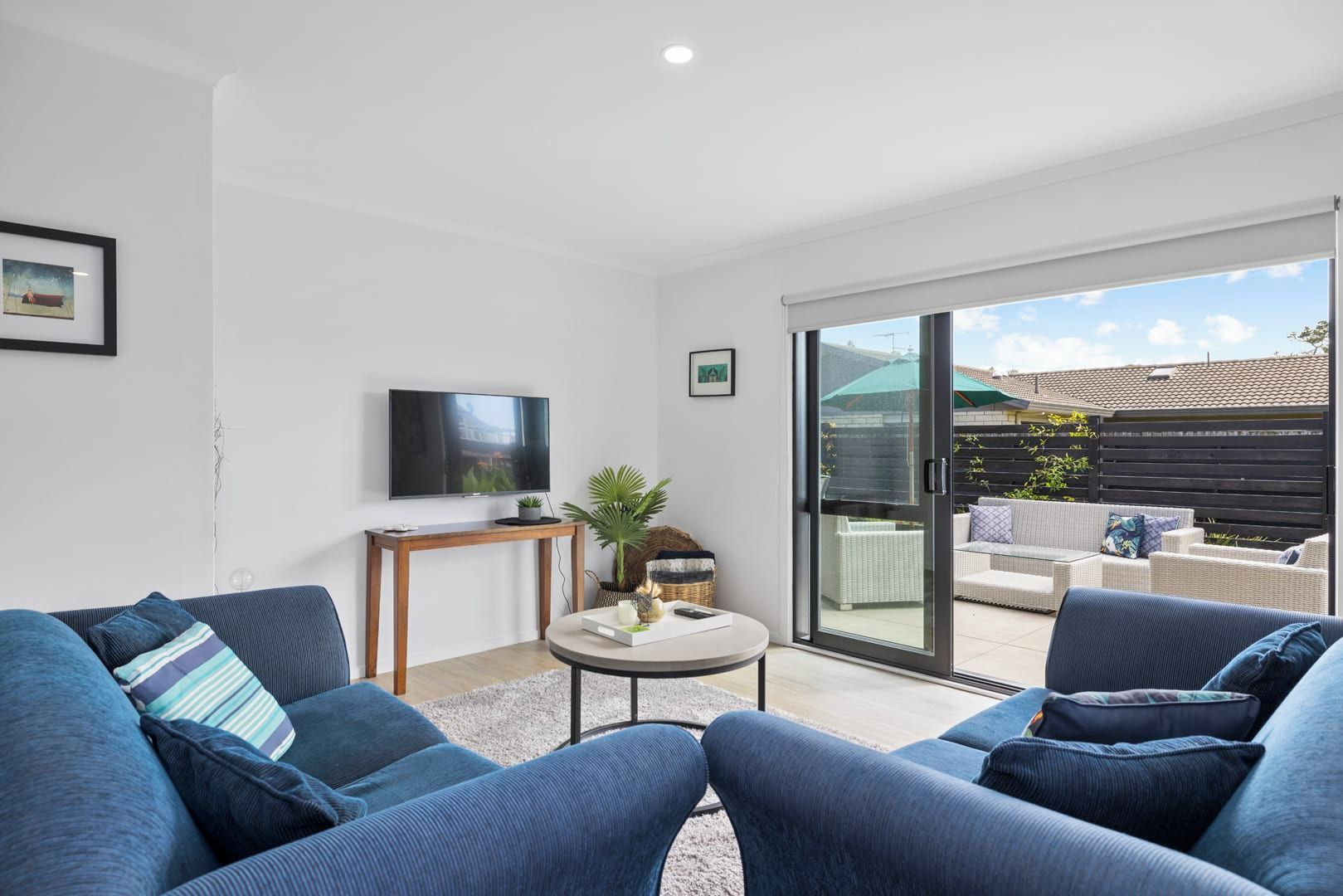 A modern living room with a flat-screen TV, a round coffee table, and blue sofas.