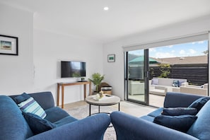 A modern living room with a flat-screen TV, a round coffee table, and blue sofas.