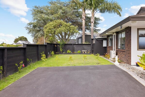 A residential property with a paved driveway leading to a front yard, a wooden fence, and a house with a brick exterior and large windows.