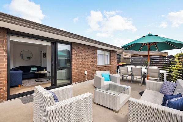 A patio area with wicker furniture, a dining table, and a green umbrella. - Mount Maunganui Getaway: Waitui Wonder House (Mount Maunganui)