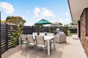 An outdoor patio with a table and chairs, a grill, and a green umbrella.