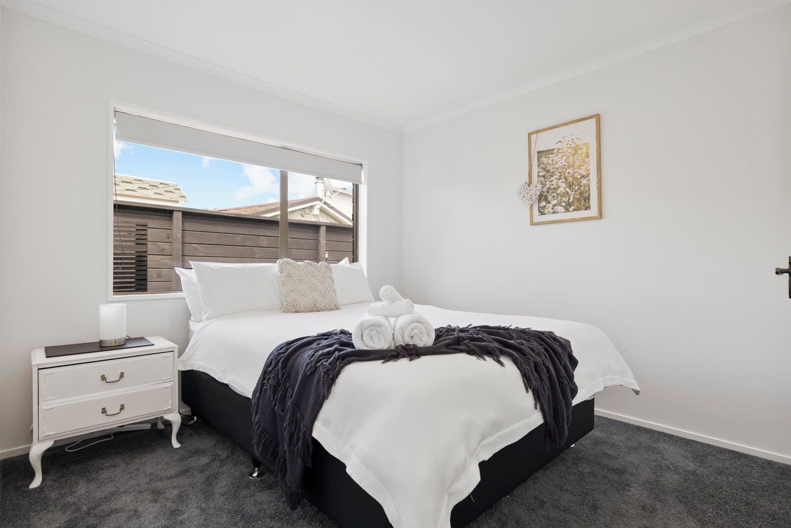 A bedroom with a bed, a nightstand, a window, and a framed picture on the wall.