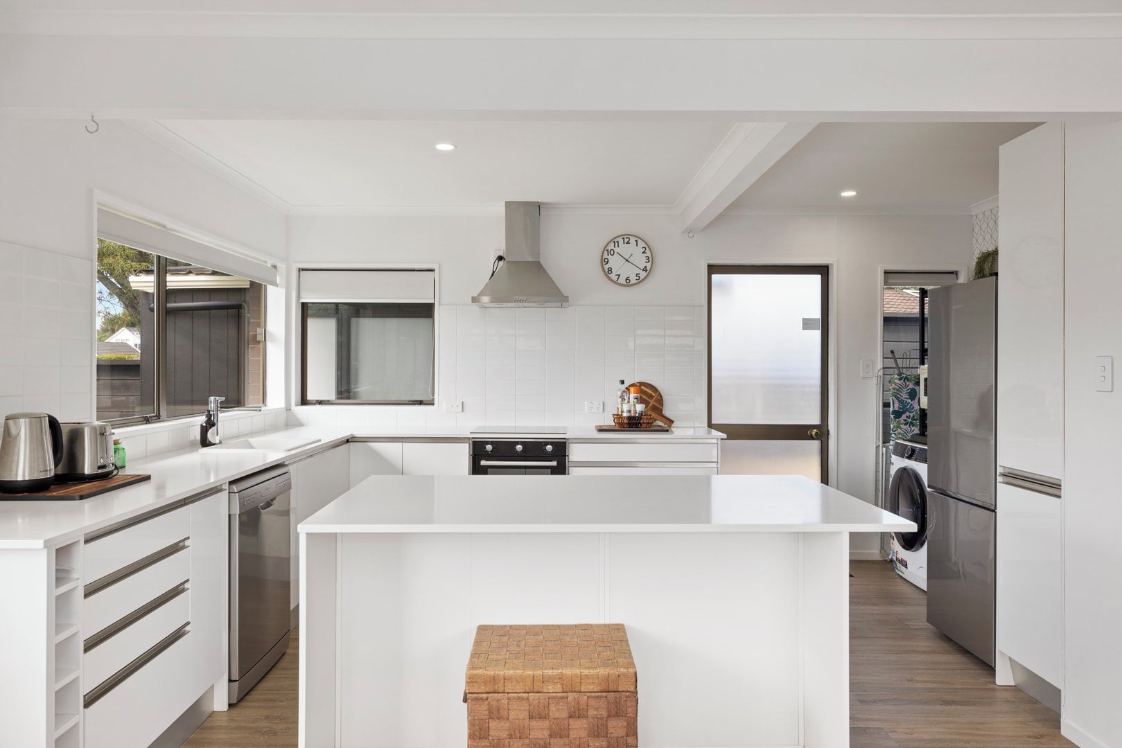 A modern kitchen with white cabinetry, stainless steel appliances, a large island, and a built-in oven.