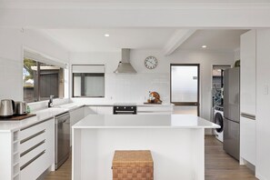 A modern kitchen with white cabinetry, stainless steel appliances, a large island, and a built-in oven. - Mount Maunganui Getaway: Waitui Wonder House (Mount Maunganui)