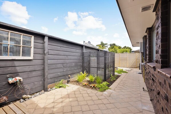 A backyard with a wooden fence, a small garden area with plants, and a bicycle leaning against the fence. - Mount Maunganui Getaway: Waitui Wonder House (Mount Maunganui)