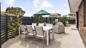 Um pátio externo com mesa, cadeiras, churrasqueira e um guarda-sol verde.