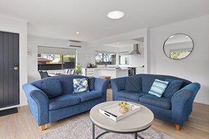A modern living room with two blue sofas, a round coffee table, and a kitchen in the background.