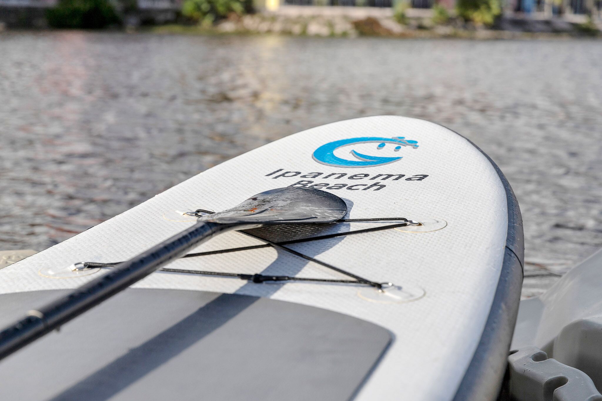 A white paddleboard with the text "Ipanema Beach" and a logo, featuring a paddle and a black handle.