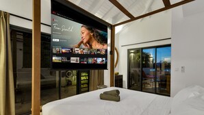 A modern hotel room with a large flat-screen TV displaying a Netflix interface, a neatly made bed, and a sliding glass door leading to a balcony. - Luxury villa overlooking the Laguna Marina (Kralendijk)