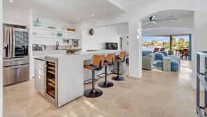 A modern kitchen with a central island, bar stools, and a dining area with a sofa and table. - Luxury villa overlooking the Laguna Marina (Kralendijk)