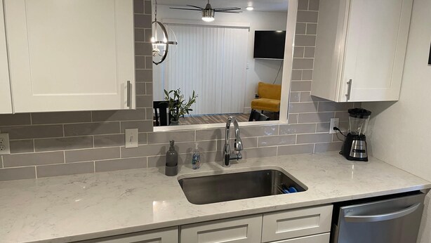 A modern kitchen with white cabinets, a stainless steel sink, a blender, and a dishwasher. - Casa Wooten -Contemporary Condo (Austin)