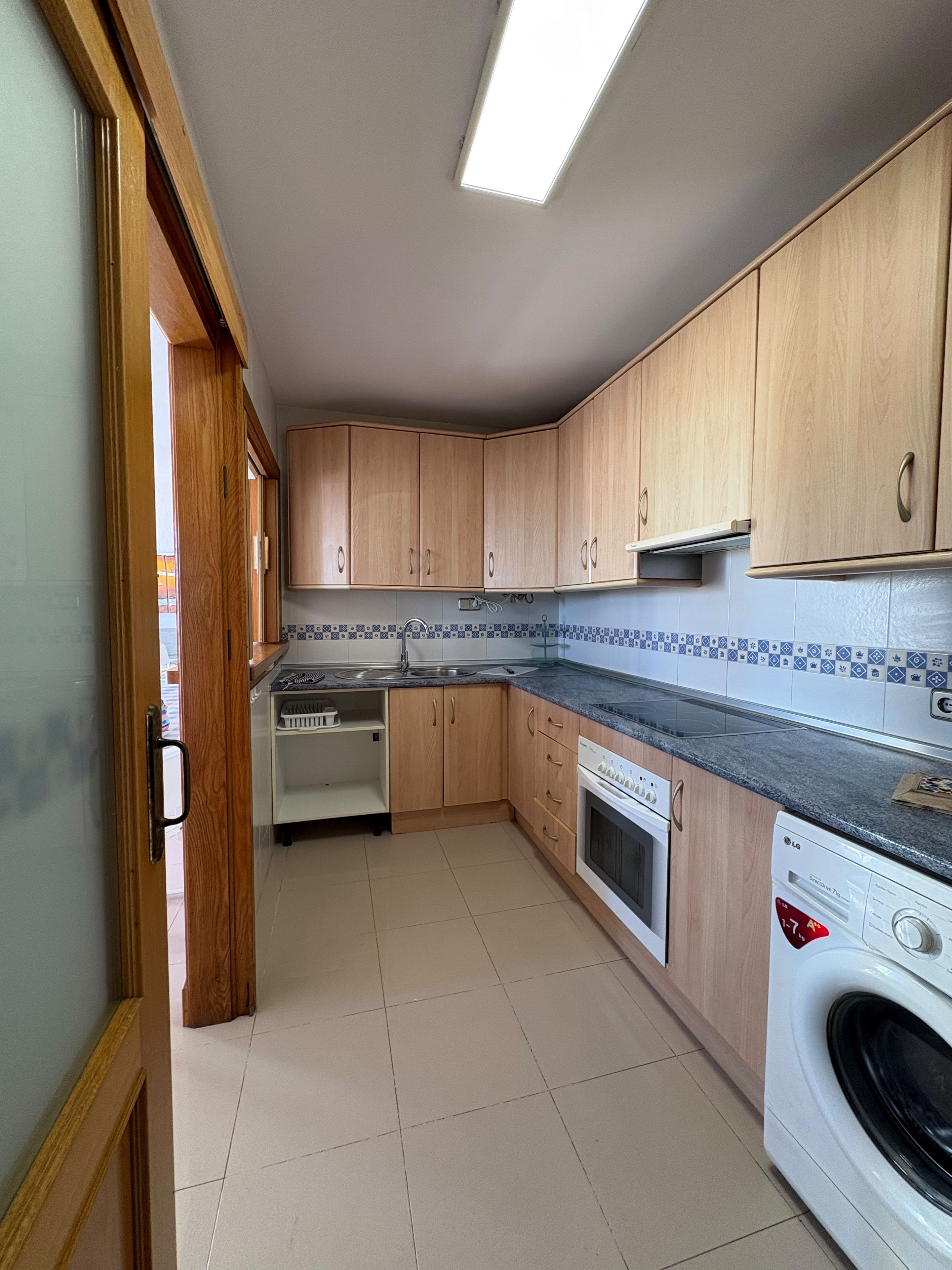 Una cocina con armarios de madera, horno empotrado, lavavajillas y lavadora.
