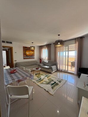 Amplia sala de estar con sofá, mesa de comedor y sillas, un ventanal con cortinas y una lámpara de techo.