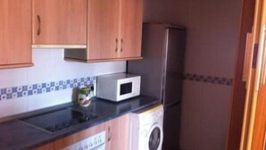 Une cuisine compacte avec des meubles en bois, un four à micro-ondes, un réfrigérateur et un lave-linge.