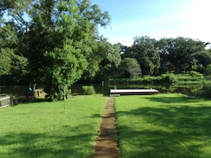 A grassy area with a pathway leading to a white structure, surrounded by trees and a body of water.