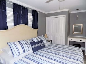 A bedroom with a bed, a desk, a wardrobe, and a ceiling fan.
