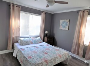A bedroom with a bed, curtains, a nightstand, a lamp, and a ceiling fan.