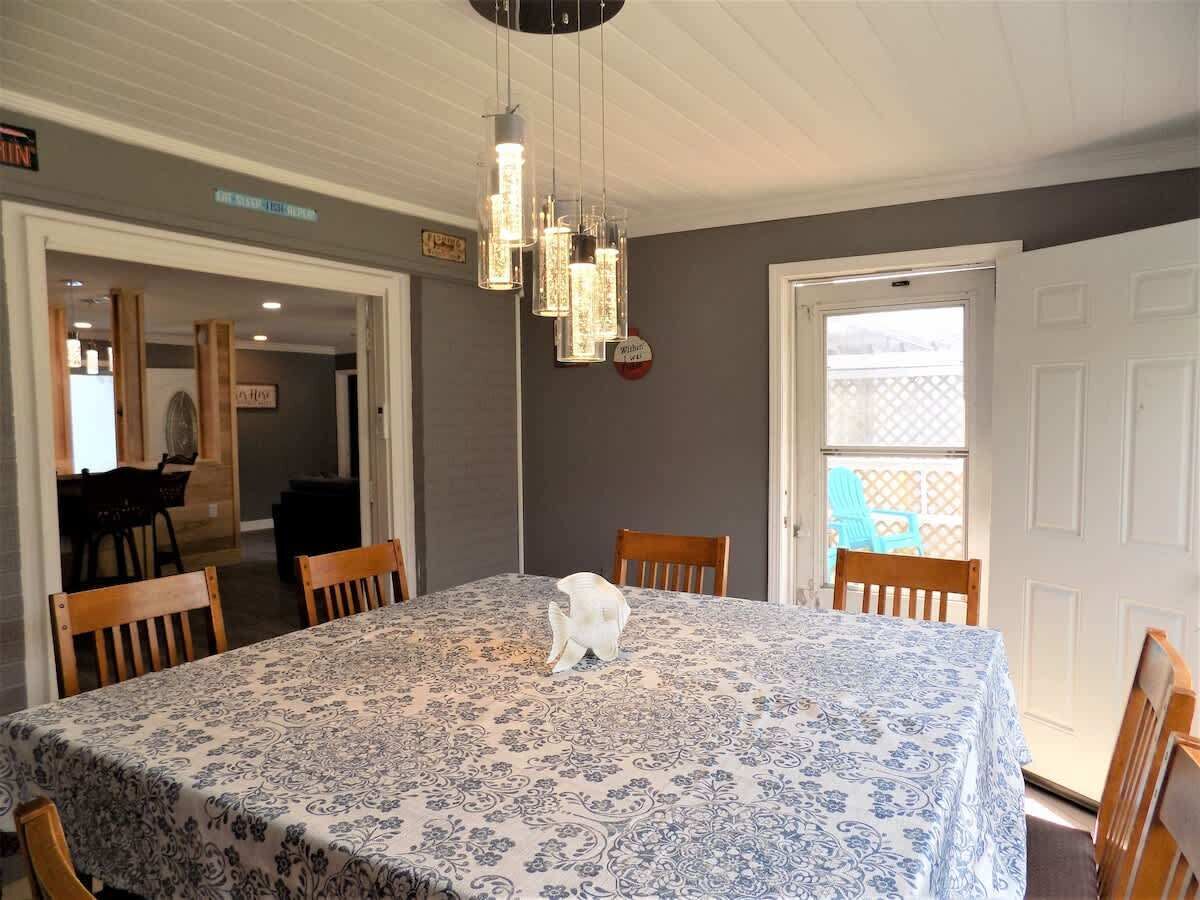 Un comedor con una mesa dispuesta para cuatro, una lámpara colgante y vistas a un área exterior a través de una puerta.