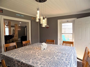 A dining area with a table set for four, a hanging light fixture, and a view through a door to an outdoor area.