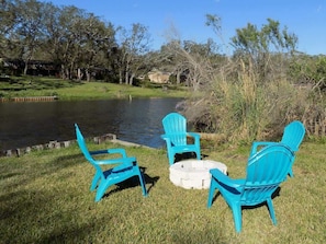 Outdoor seating with chairs and a stone fire pit by a pond.