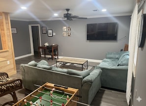 A living room with a foosball table, a sofa, a television, and a ceiling fan.