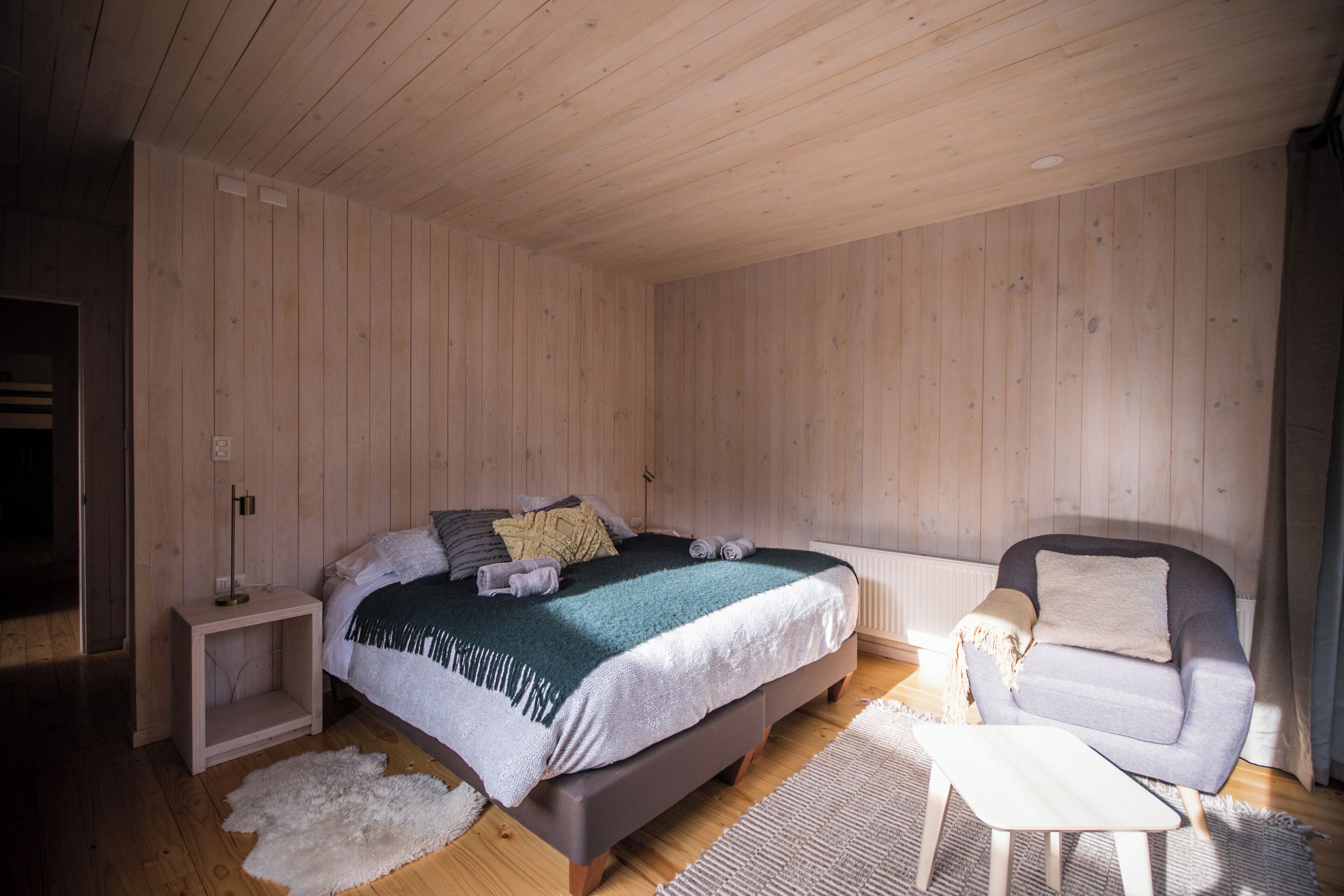 A bedroom with a bed, a chair, a small table, and a white rug.