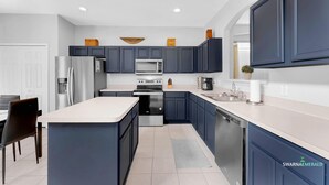 A modern kitchen with dark blue cabinets, a white countertop, stainless steel appliances, and a built-in dishwasher. - Near Disney with Themed Rooms, Pool & Hot Tub (Kissimmee)