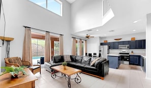 A spacious living area with a black leather sofa, a wooden coffee table, and a dining table with chairs. There is a kitchen with dark blue cabinets and modern appliances. - Disney Hideaway: Private Pool & Overflowing Spa (Kissimmee)