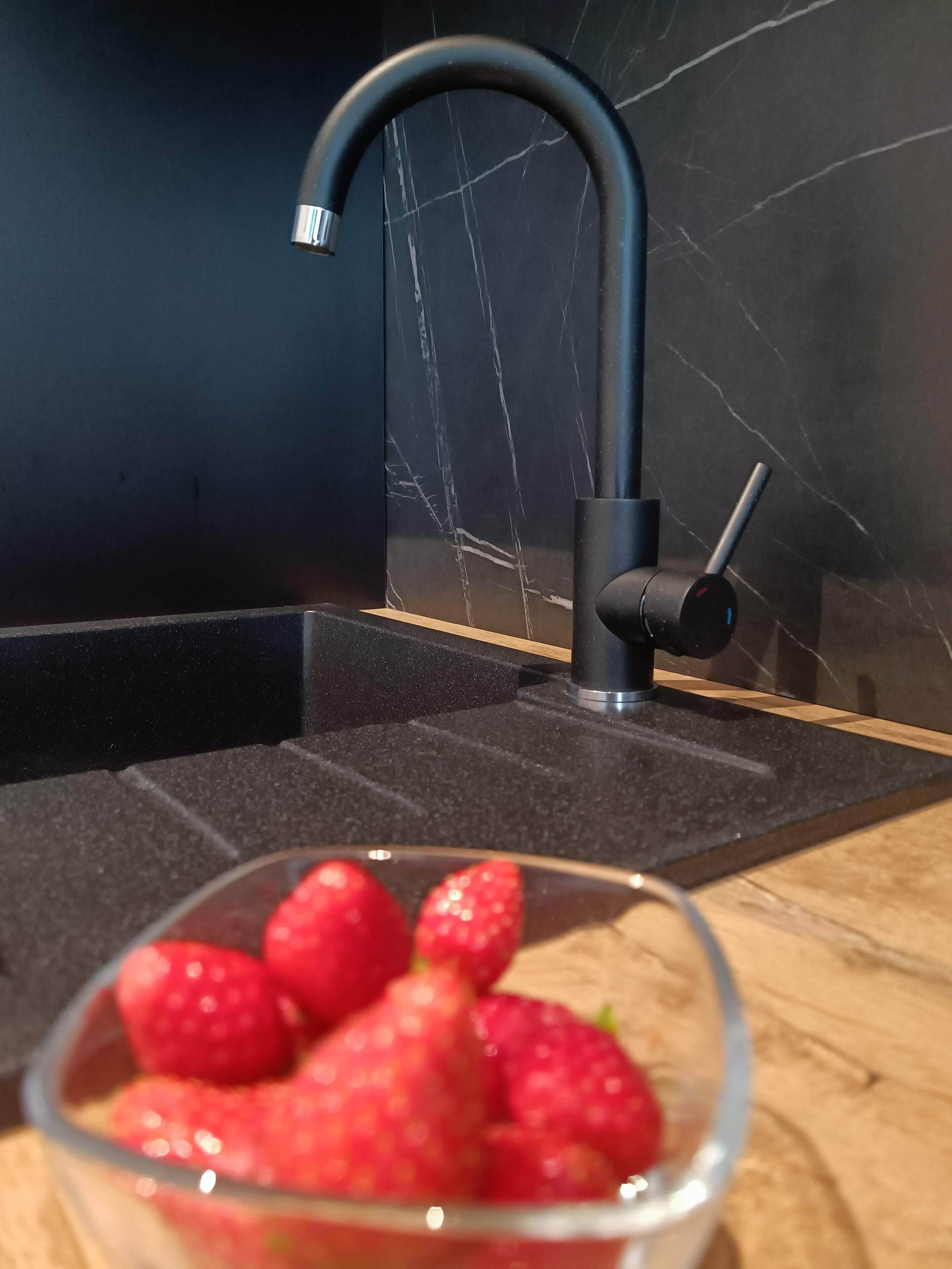 Una cocina moderna con encimera de mármol negro, un grifo negro elegante y un cuenco de fresas.