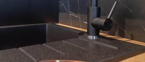 Una cocina moderna con encimera de mármol negro, un grifo negro elegante y un cuenco de fresas.