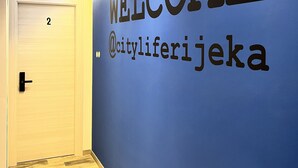 A hallway with a blue wall featuring a large "WELCOME" sign and a Twitter handle "@cityliferijke". - City Life Rijeka (Rijeka)