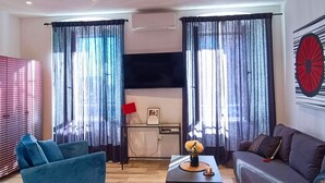 A modern living room with a sofa, a blue armchair, a coffee table with a vase, and a flat-screen TV mounted on the wall. - City Life Rijeka (Rijeka)