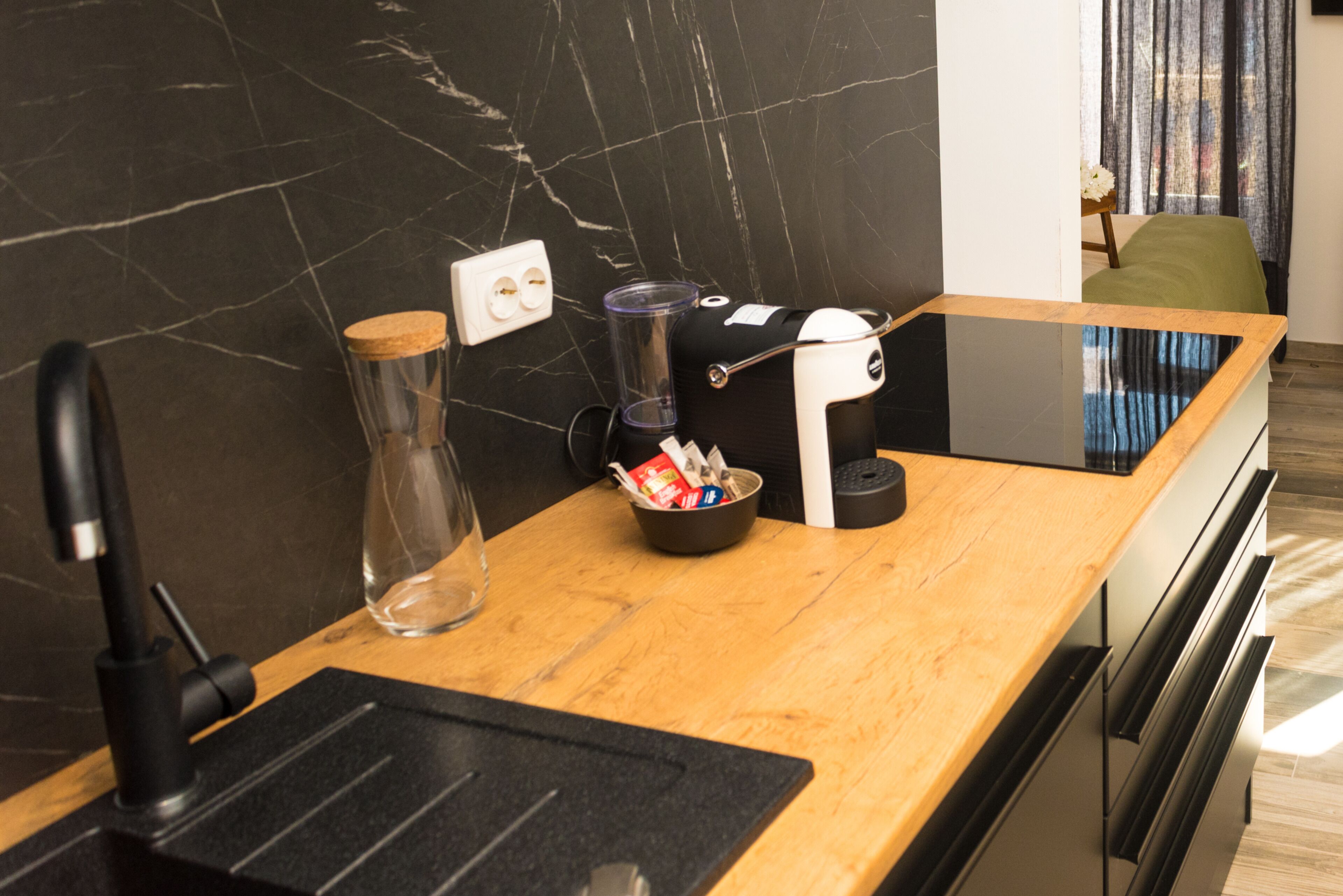 Een moderne keuken met een marmeren spatwand, een koffiezetapparaat, een glazen pot en een schaal met snacks.