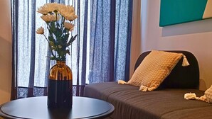 A modern living room with a dark sofa, a round table with a vase of flowers, and a large window with curtains. - City Life Rijeka (Rijeka)