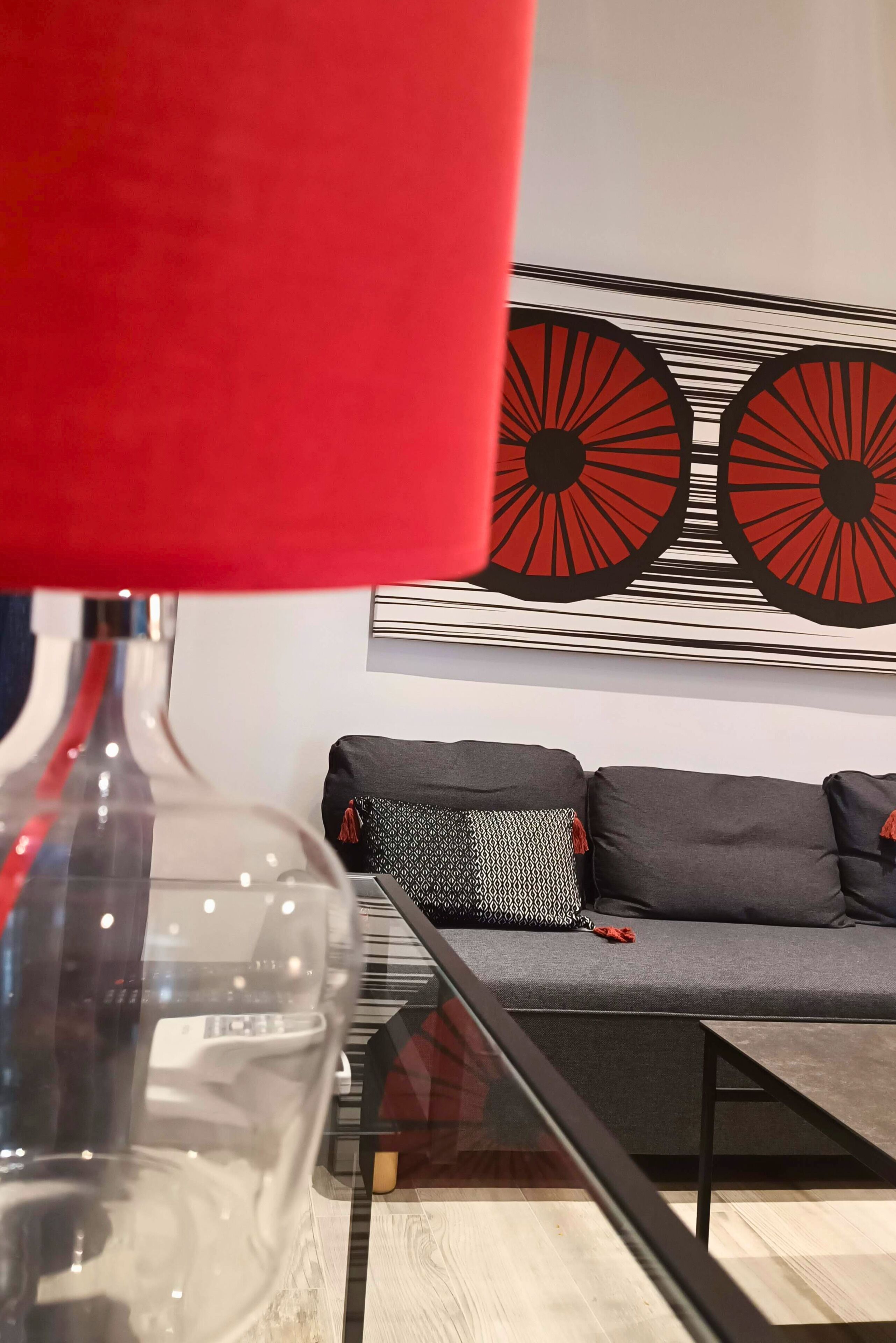A modern living room with a sofa, a glass coffee table, and a red lamp.