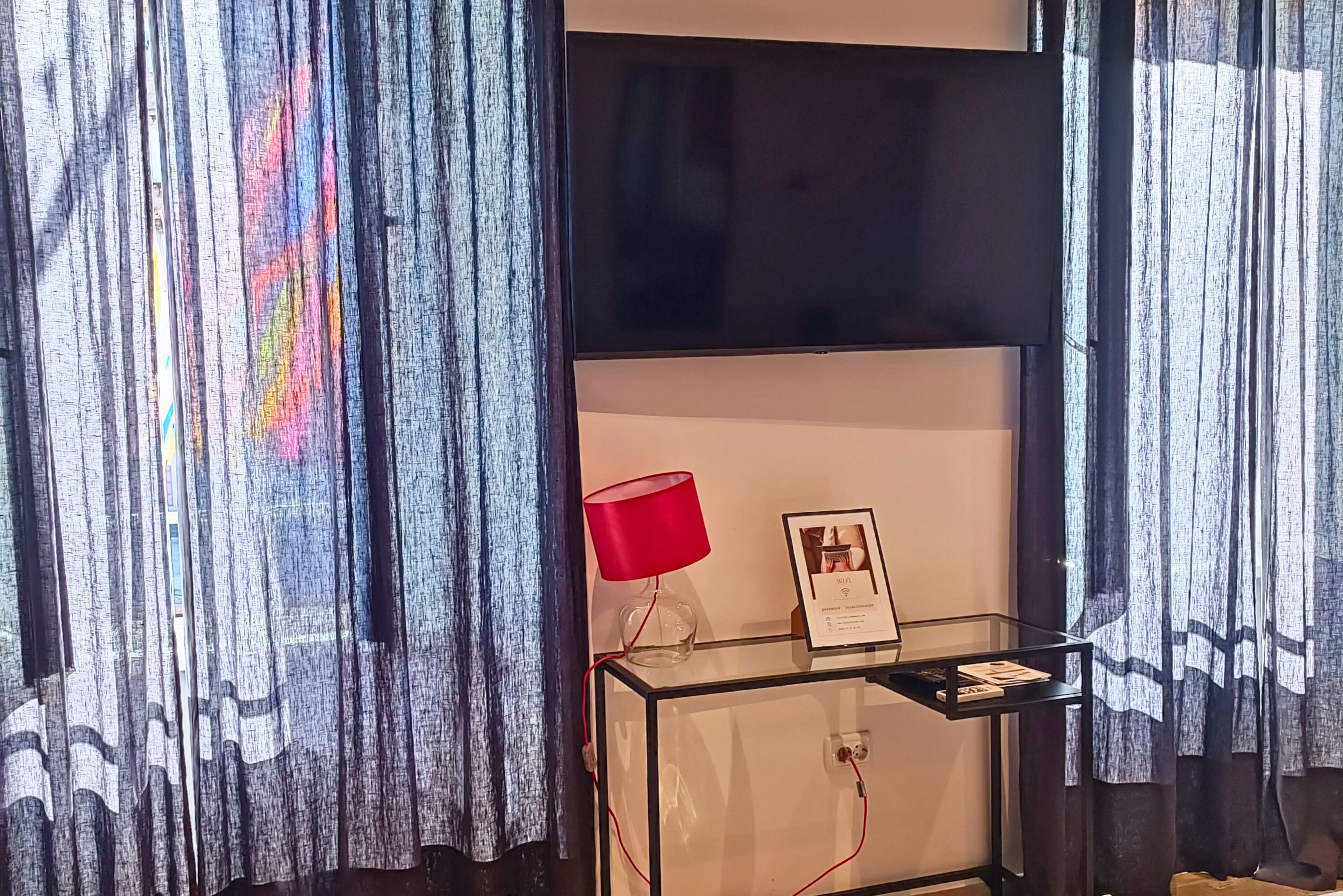 Una habitación con un mueble de televisión de vidrio, una lámpara roja y un cuadro enmarcado.