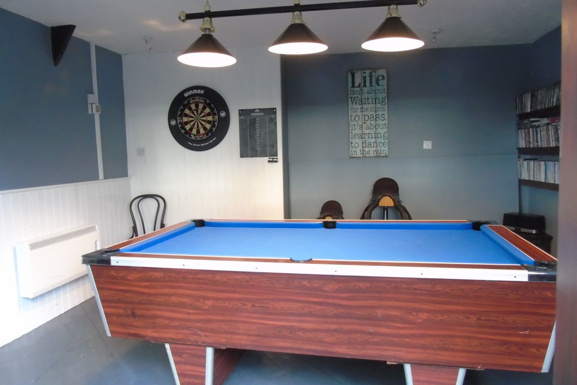 A pool table in a room with a dartboard and a motivational quote on the wall.