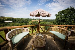 A wooden deck with two cushioned chairs and a table, an umbrella, and a view of a lush landscape. - Cuckoo's Nest - Dog Friendly Cottage with a hot tub sleeping 6-8 (Umberleigh,)