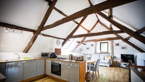 Eine gemütliche Dachküche mit freiliegenden Holzbalken, einem Essbereich mit einer Couch und einem Fernseher.