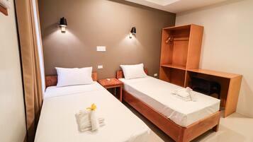Hotellihuone, jossa on kaksi erillistä sänkyä, puinen vaatekaappi ja kaksi seinälle asennettua lamppua.