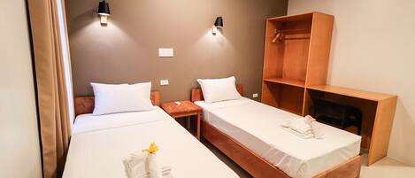 A hotel room with two single beds, a wooden wardrobe, and two wall-mounted lamps.