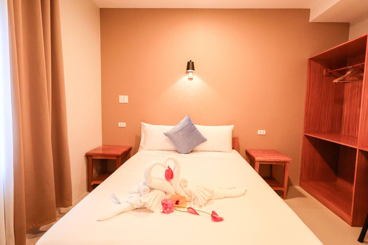 A hotel room with a bed, a nightstand, a wooden wardrobe, and a wall-mounted light.