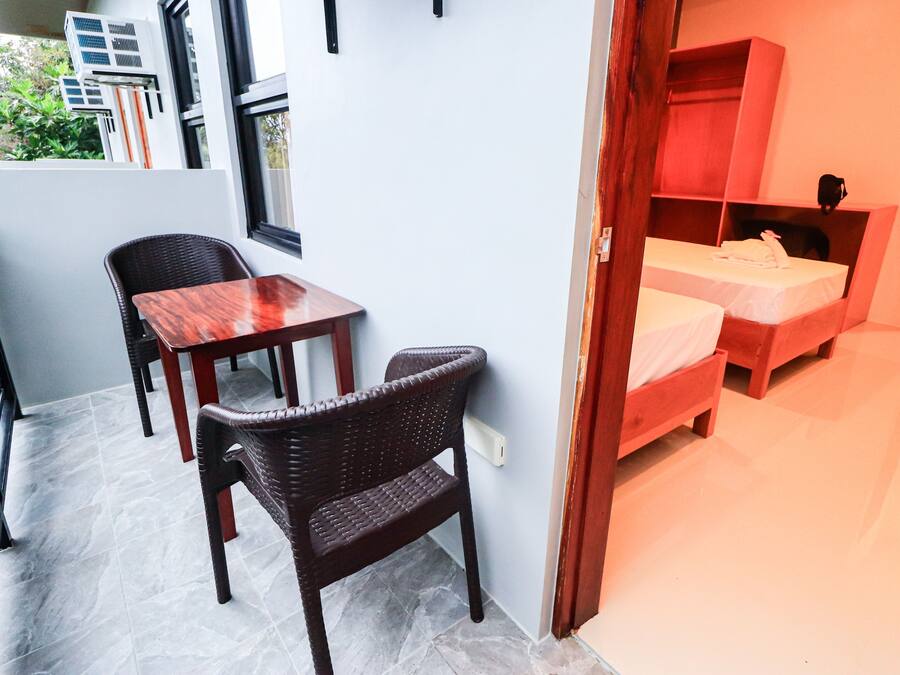 A room with a wooden table and chairs, a bed with a red headboard, and a window with air conditioning units outside.